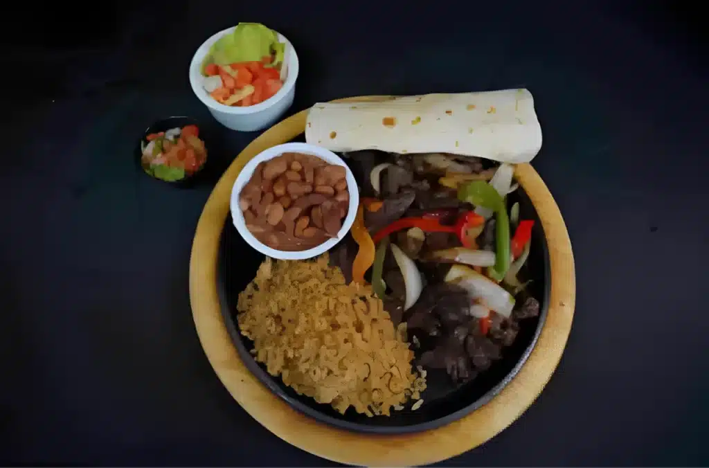 A plate of fajitas with beans, rice, tortillas, and sides of lettuce, tomatoes, and salsa.