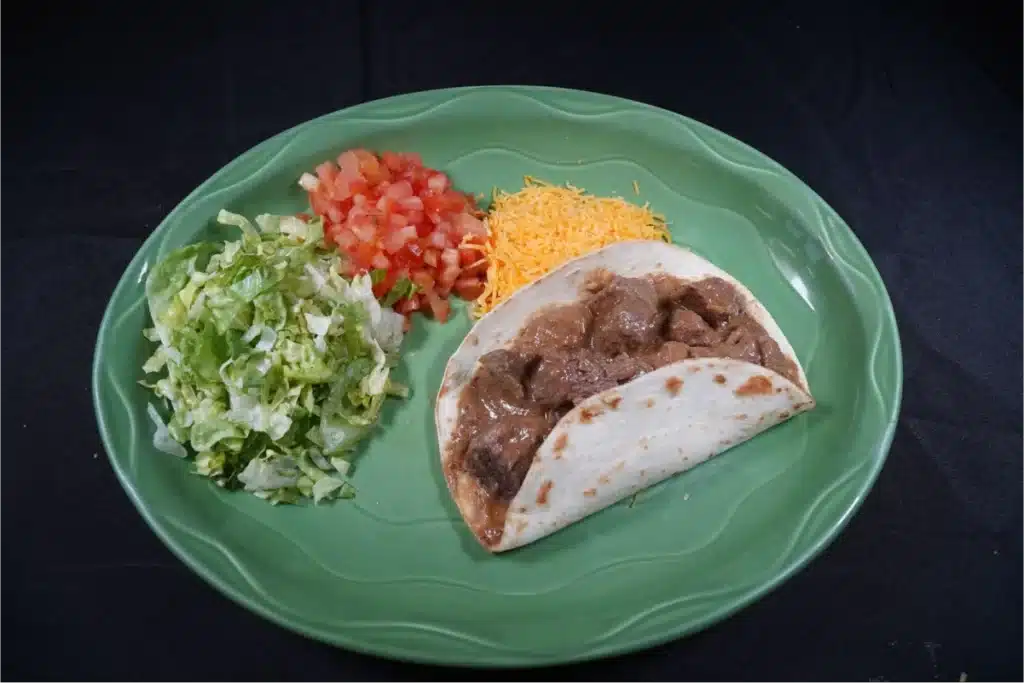 A taco with sides of lettuce, tomatoes, and shredded cheese.