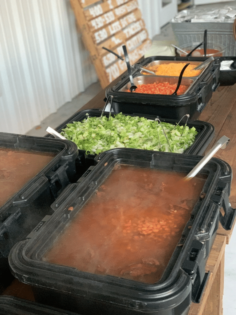 A wedding buffet with steaming trays of Tex-Mex staples like beans, shredded lettuce, and taco toppings.