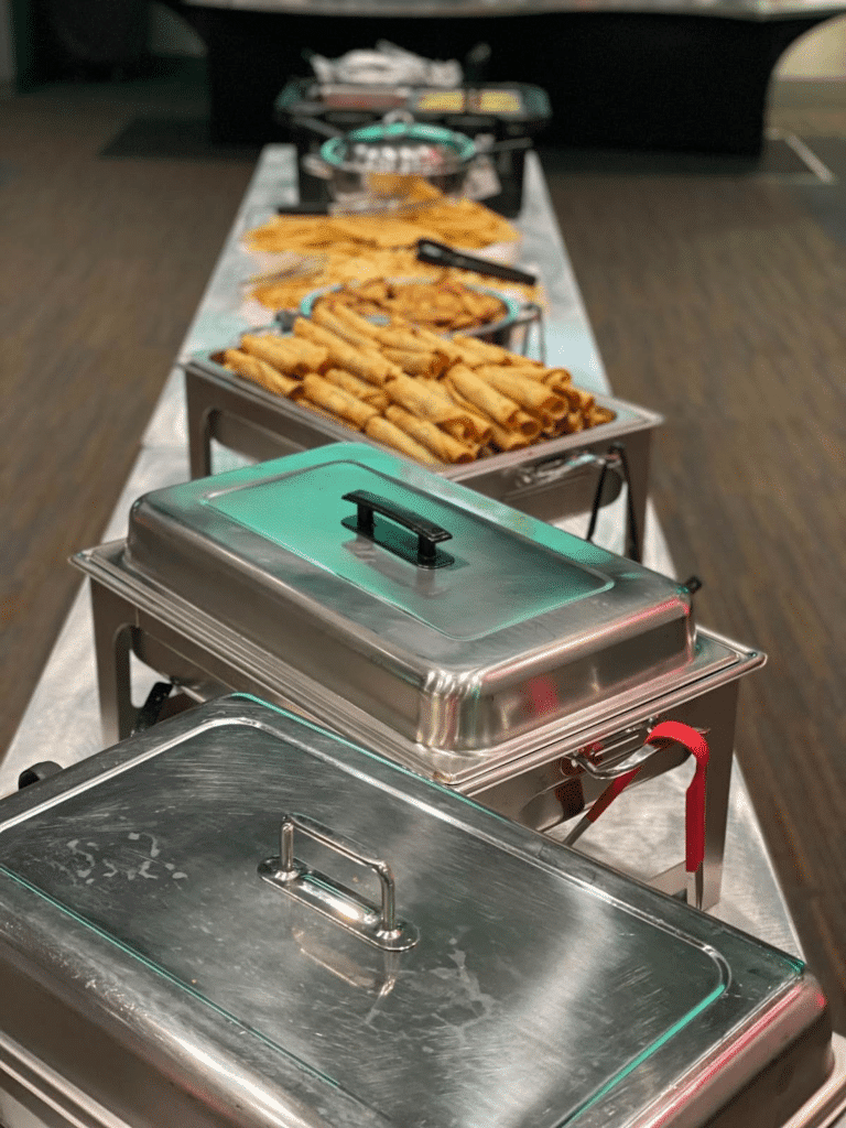 A row of catering trays filled with rolled tacos and Tex-Mex dishes at a wedding reception.