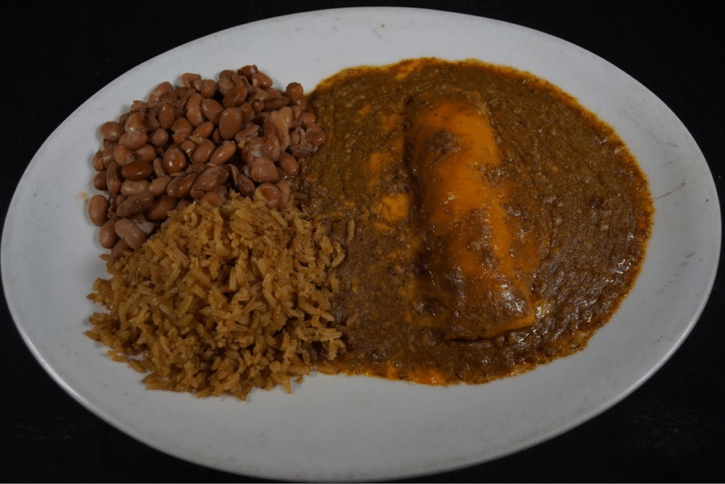 A large plate with tamales, beans, and rice covered in rich sauce.