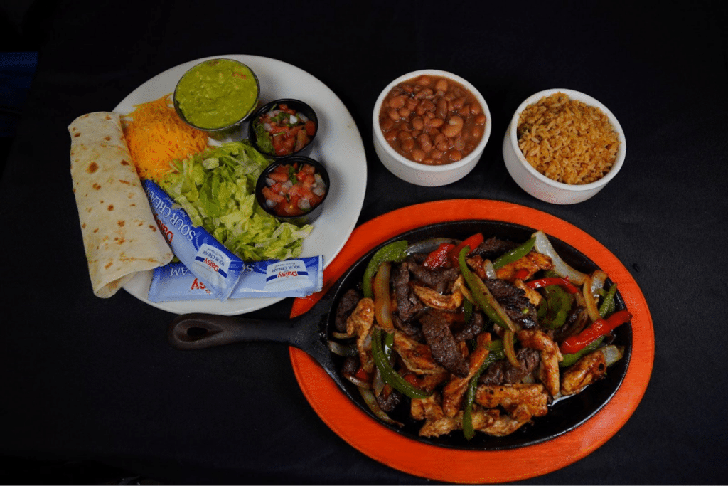 A sizzling Tex-Mex fajita platter with sides of guacamole, lettuce, and beans.